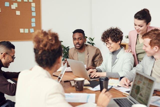 A diverse group of people in an office meeting, sitting around a desk.
