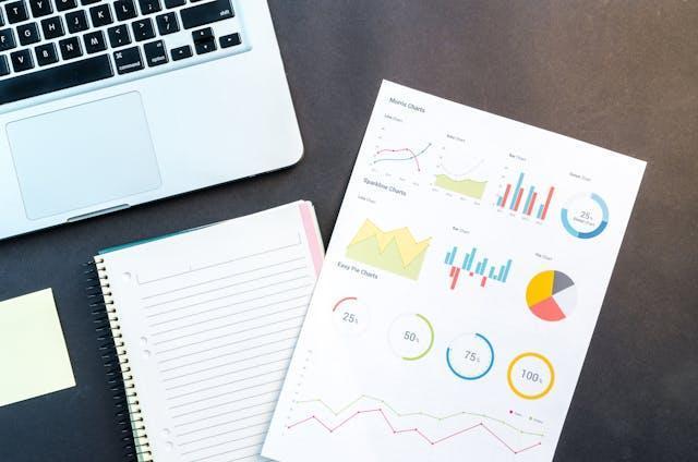 Charts and graphs on a piece of paper next to a laptop.